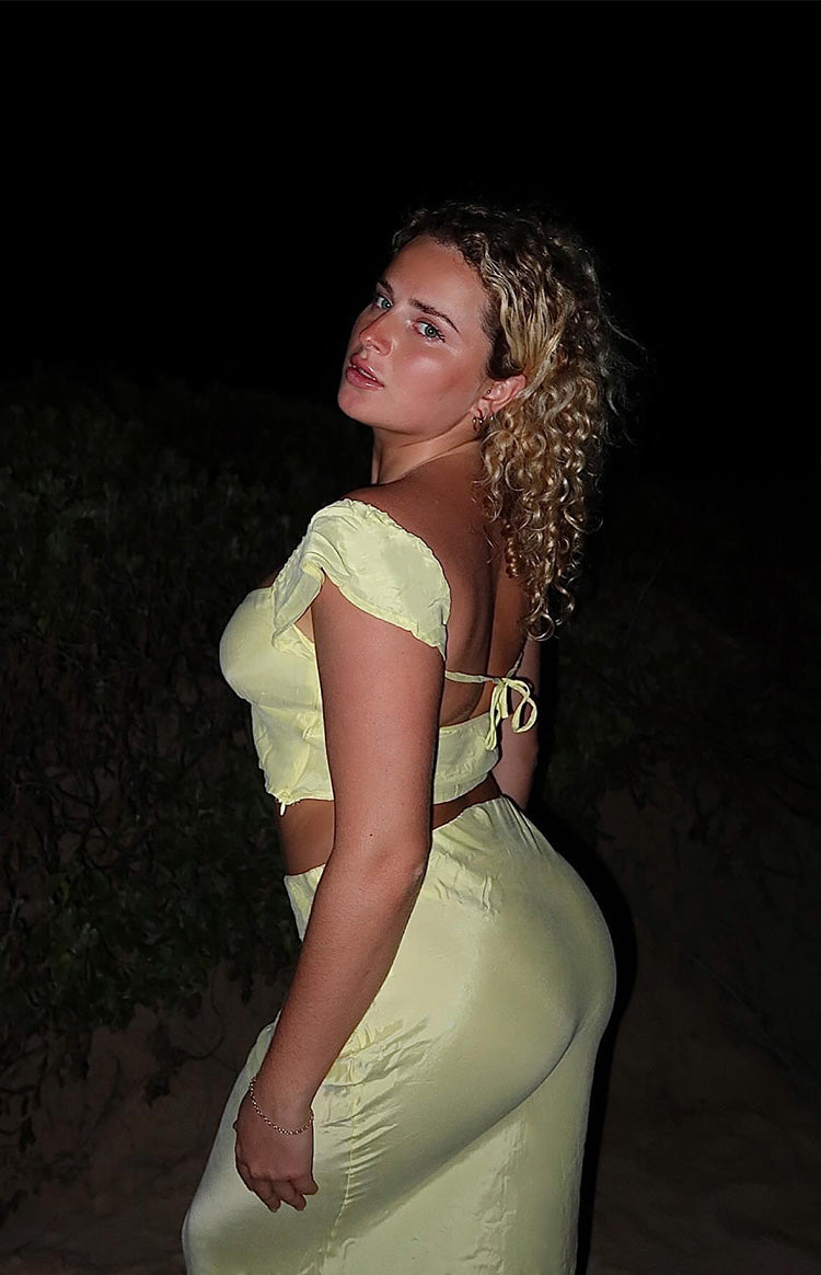Side view of a yellow crop top with off-shoulder ruched sleeves and a tie-back detail