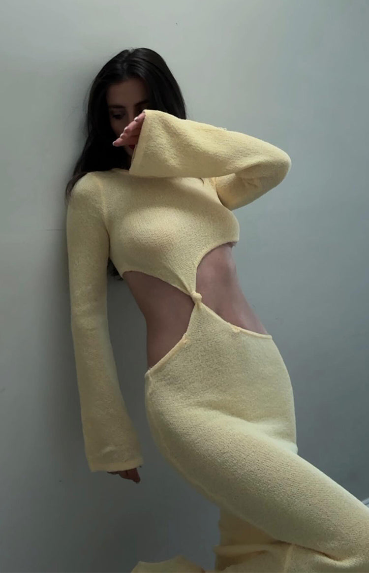 Side profile of a yellow knit maxi dress featuring large waist cutouts with a central knot and long bell sleeves