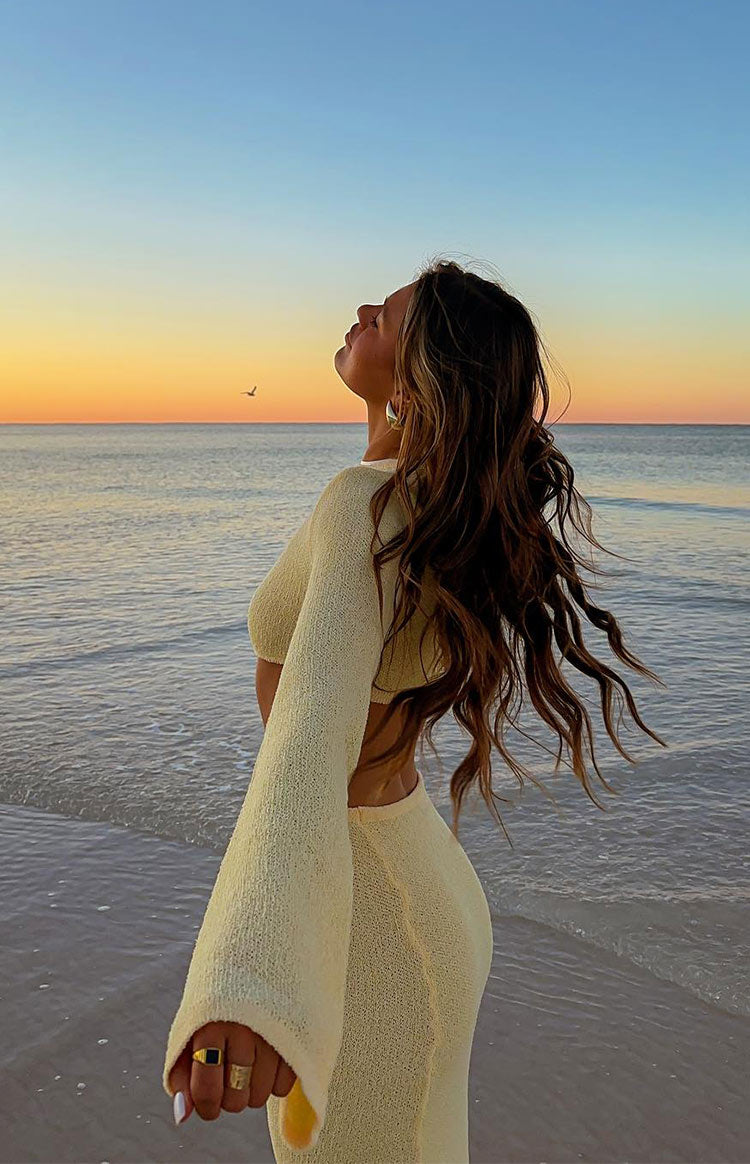 Side view of a yellow knit maxi dress with long wide sleeves, textured fabric, and a midriff cut-out