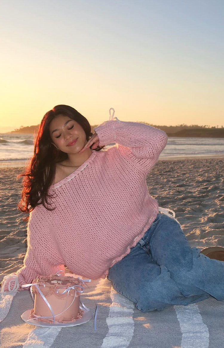 Baby pink chunky knit sweater with a boat neckline featuring white tie details and an adjustable cropped hem with white ties