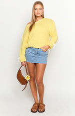 Yellow chunky knit sweater with a wide neckline, white ties on the sleeves and shoulder, and a white stitched raw hem