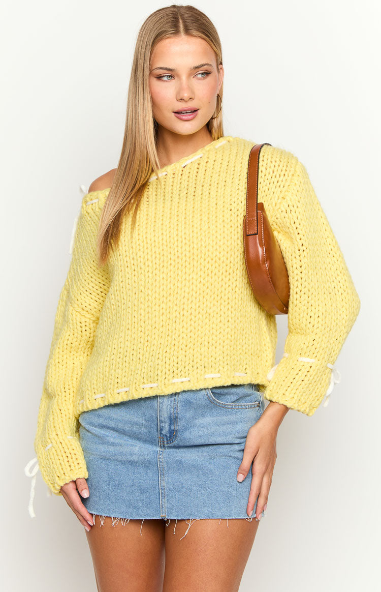 Yellow chunky knit sweater with an off-shoulder neckline, white contrast stitching, and cuff ties