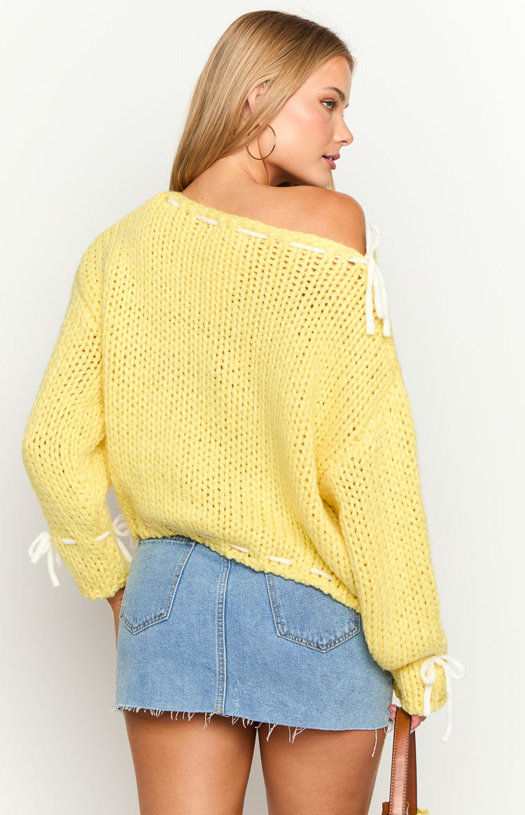 Rear view of a yellow chunky knit sweater with white tie details on the off-shoulder neckline and cuffs