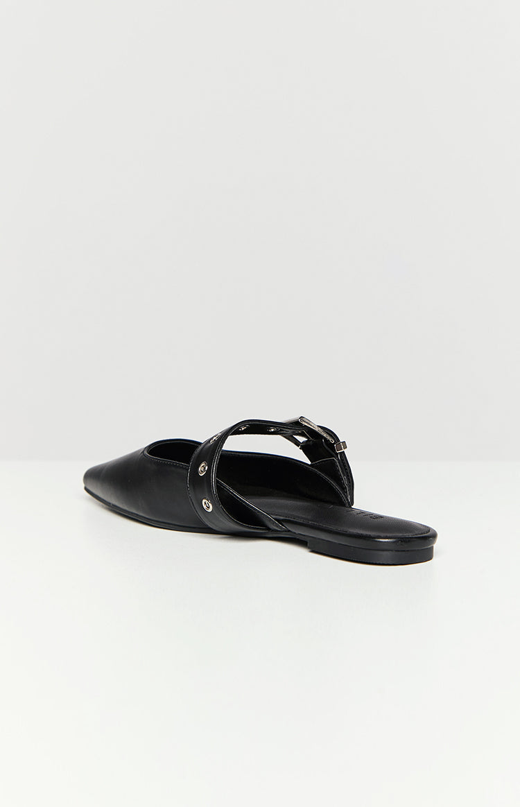 Side-rear view of a black mule with a pointed toe, flat sole, and a back strap featuring silver eyelets and a buckle