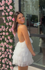 Side view of a white halter neck mini dress with a low open back and tiered ruffled tulle skirt