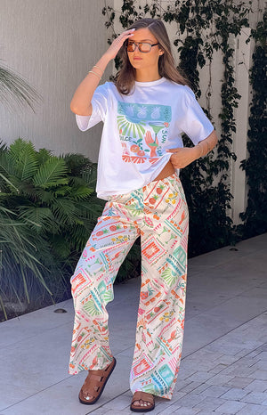 Full-length view of white wide-leg pants with a colourful Dolce Vita print featuring pineapples and cocktails