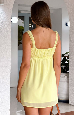 Rear view of the yellow mini dress showing shirred straps, a square back, elasticated waist, and sheer hem