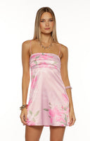 Our model wearing a mini slip dress in a light pink satin fabric. This dress is printed with a subtle large-scale pink and pale green floral design. It features a straight neckline with a draped band across the bust and is supported by very thin spaghetti straps.