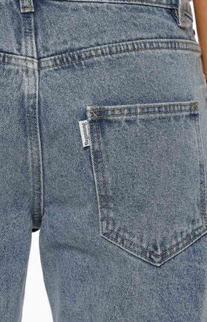A close-up shot focuses on the back hip and pocket of a pair of our light wash denim jeans. This denim has a acid-wash texture with visible seams in an brown stitching and a large square back pocket.