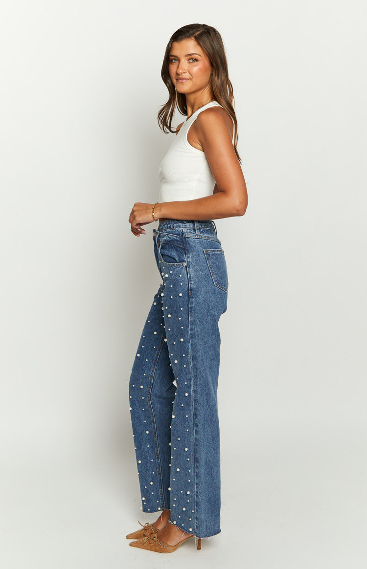 Side view of mid-wash high-waisted jeans with pearl embellishments down the legs and a raw hem