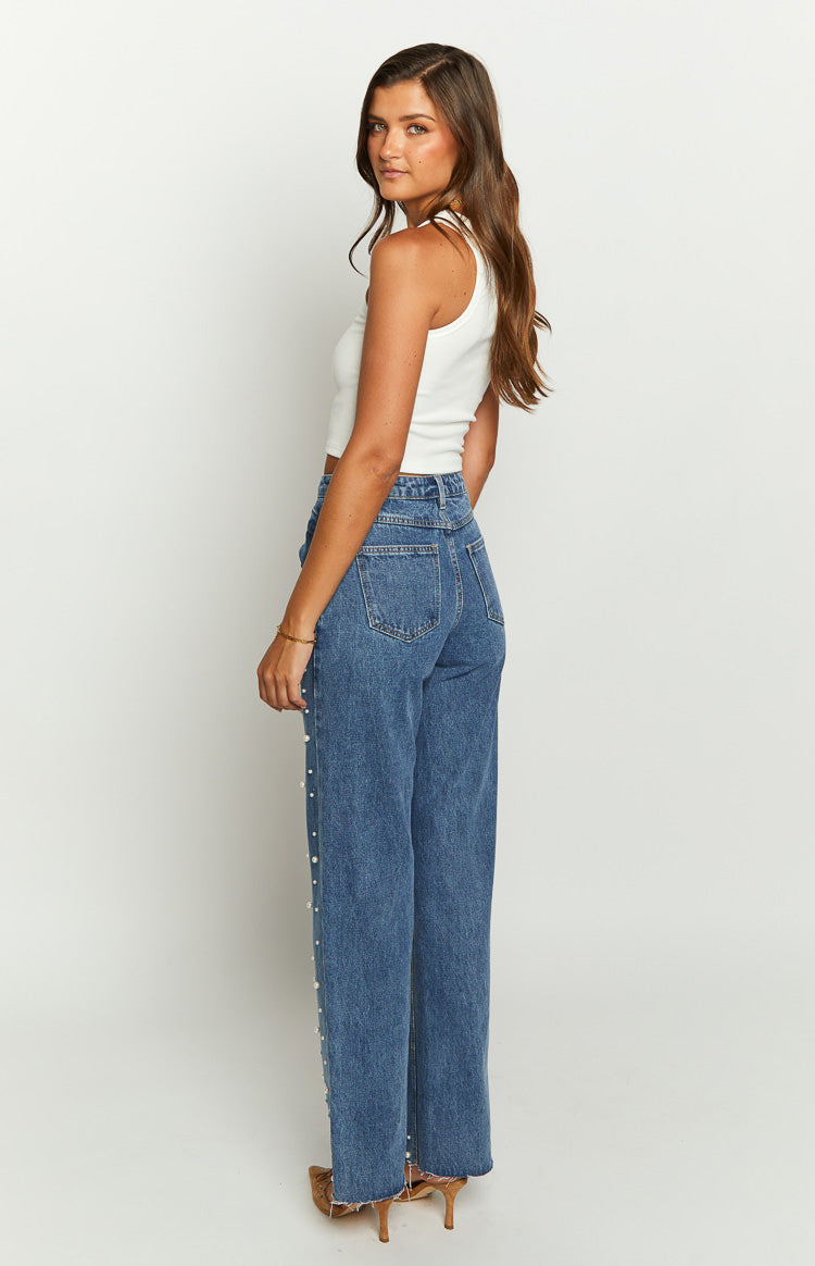 Side view of mid-wash high-waisted jeans with pearl embellishments down the legs and a raw hem