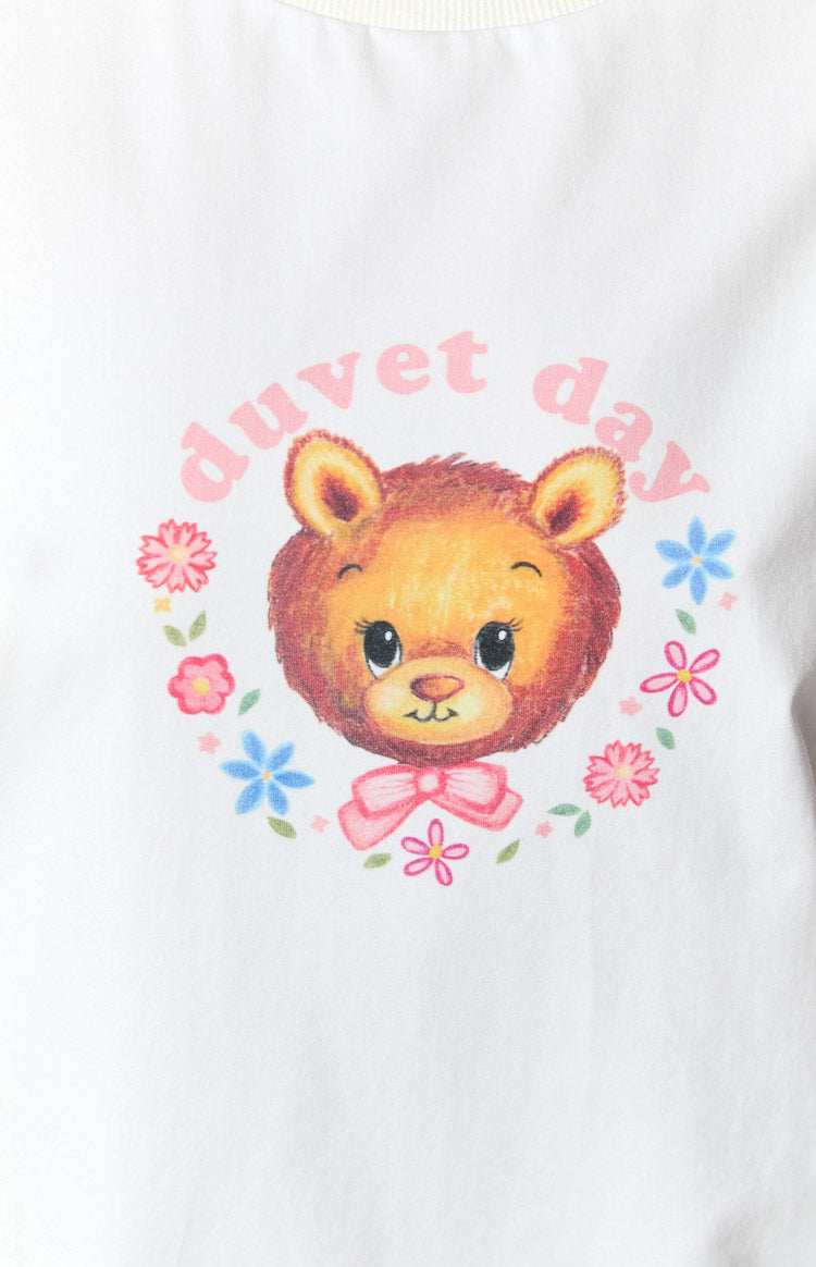 Close-up of the graphic print featuring a cartoon bear head, pink duvet day text, and floral wreath on a white tee