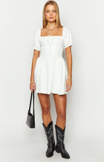 Front view of a white mini dress with a square neckline, tie detail, short puff sleeves, and a ruched skirt
