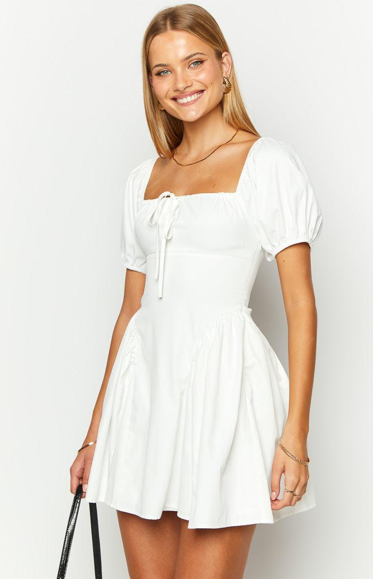 White mini dress with a square neckline, front tie detail, short puff sleeves, and a gathered skirt