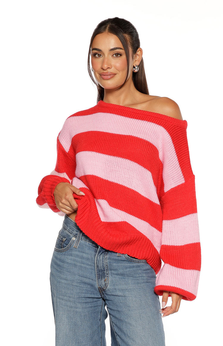 Off-shoulder neckline of a red and pink striped knit sweater with a relaxed fit