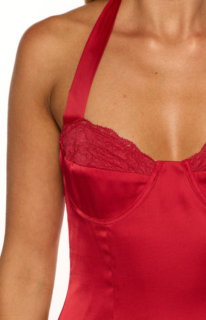 Our model wearing a short red mini dress made of a shimmering satin fabric. This mini dress features a halter neckline and a sweetheart bustier-style bust accented with a delicate lace trim along the top edge. The skirt has a slight A-line flare and falls high on the thigh.