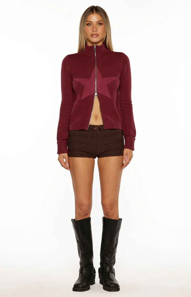 Cropped burgundy knit sweater with a prominent star pattern on the front and high zip neck