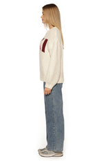 Side view of a cream chunky knit sweater with a relaxed fit and long sleeves, showing the burgundy jacquard pattern