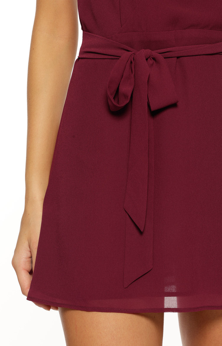 Close-up of the tied waist sash on a burgundy mini dress with a subtle sheer hem