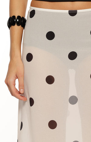 Our model is wearing a sheer white midi skirt with a black polka dot pattern. This skirt features a fitted thin white waistband and an asymmetrical hemline with a pointed handkerchief corner that falls below the knee.