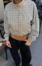 Front view of a beige plaid funnel neck jacket with a silver front zipper, vertical stitched detail, and elasticated cropped