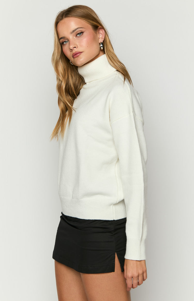 Side view of a cream turtleneck sweater showing the relaxed fit and ribbed cuffs