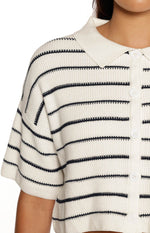 A close-up image of a cropped cream-colored knit polo shirt featuring thin horizontal navy blue stripes. The top has short sleeves with dropped shoulder seams a white fabric collar (contrasting slightly with the knit body) and a central button placket with large round white buttons. The knit texture is clearly visible.