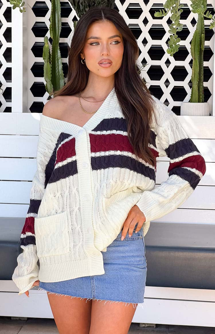 Front view of a cream cable knit cardigan with burgundy and navy stripes, V-neck, button front, and patch pockets