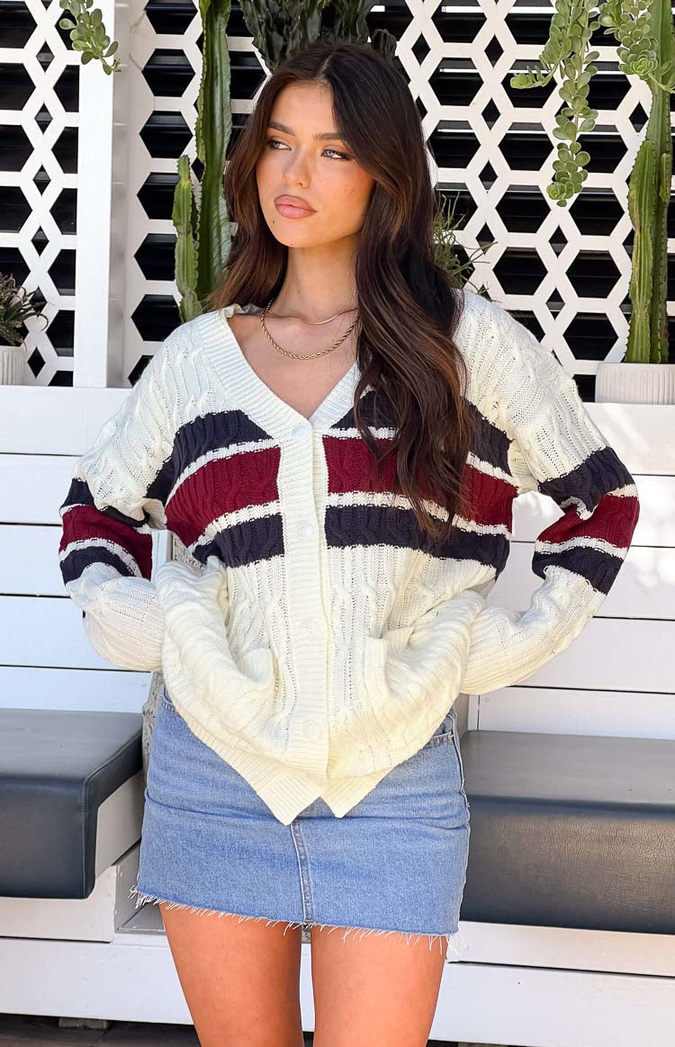 Cream cable knit cardigan with V-neck, white button-front, and burgundy and navy stripes