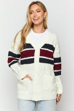 Front view of a cream cable knit cardigan with burgundy and navy stripes, V-neck, button-front, and front pockets