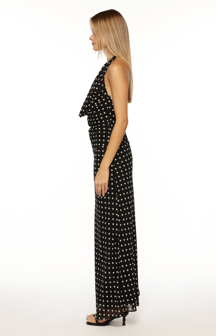 Side view of a black polka dot maxi dress showing the draped cowl neck and flowy skirt