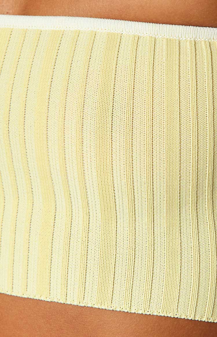 Mid-shot of a yellow ribbed knit tube top featuring white contrast binding on the strapless neckline and hem