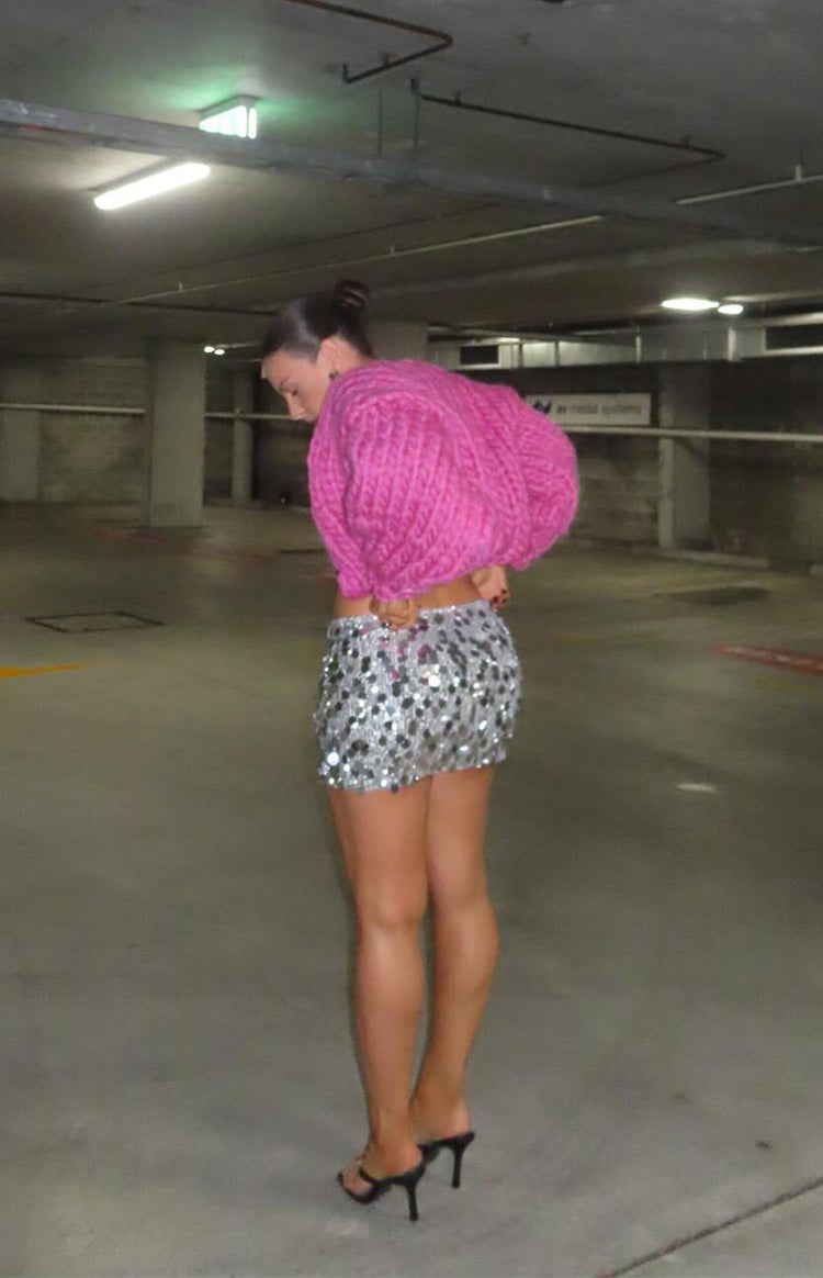 Side view of a cropped pink chunky knit cardigan with voluminous sleeves