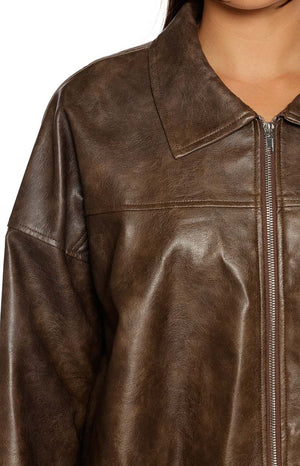 A close-up focusing on the shoulder and chest of a dark distressed brown faux leather jacket. The jacket features an oversized dropped shoulder design a classic point collar and a visible vertical silver zipper down the center. A horizontal seam across the chest adds detail to the garment.