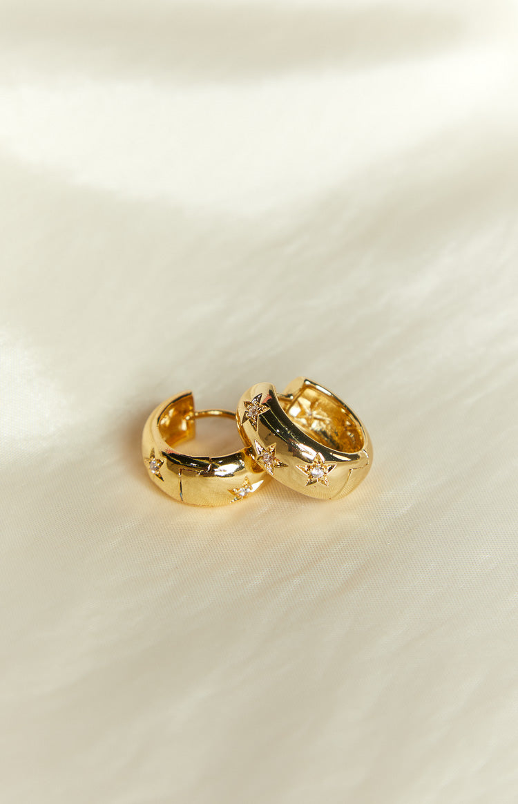Angled view of two gold hoop earrings with star cutouts and small clear stones