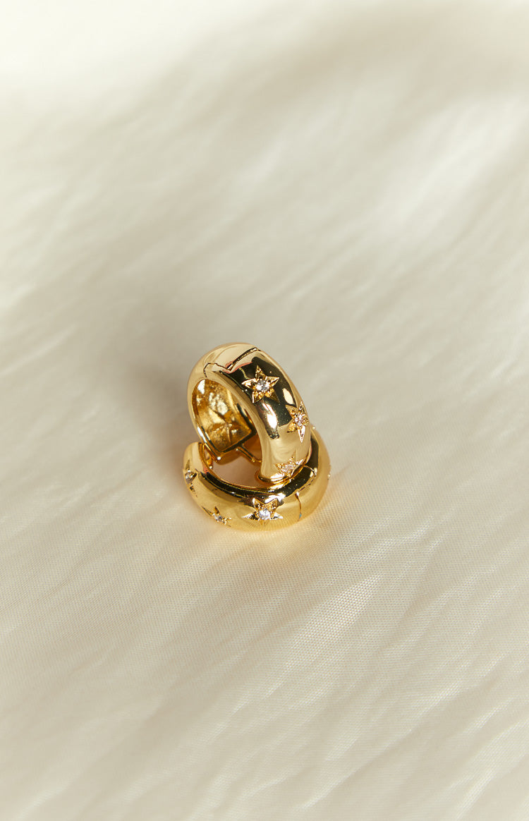 Angled view of two chunky gold hoop earrings with star-shaped diamante details