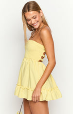 Side view of a yellow strapless mini dress with a smocked bodice, side cutouts, and a ruffled hem