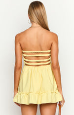 Rear view of a yellow mini dress with four horizontal elasticated straps across the back and a ruffled hem