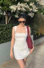 Front view of a white mini dress with a square neckline, pink bow shoulder straps, and lace trim