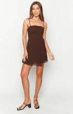 Front view of a brown mini dress with a ruched bust, spaghetti straps, and a wrap-style skirt with a side tie