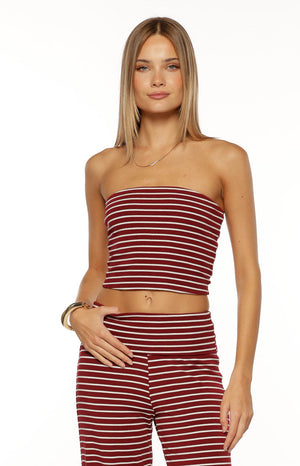 Our model is wearing a strapless bandeau crop top in a knit fabric. This top features a horizontal stripe pattern with thin white lines over a deep burgundy color. It has a tight-fitted silhouette and hits high on the midriff.