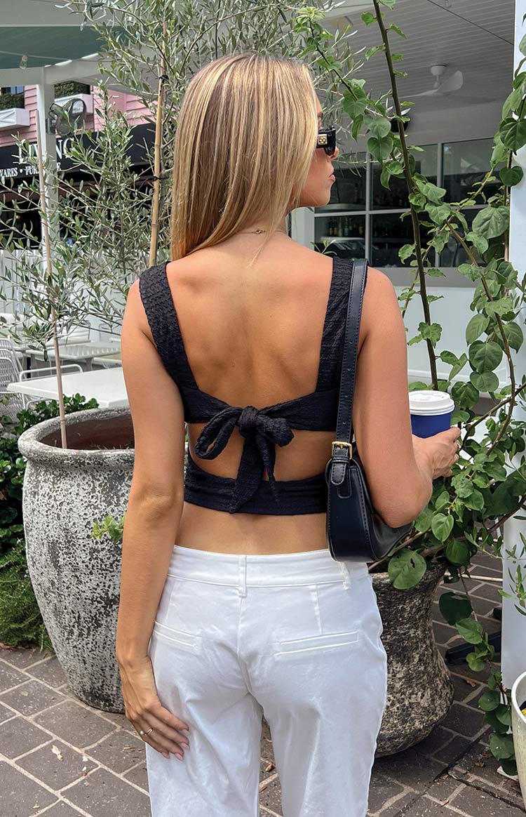 Rear view of a black textured crop top with a large tie-back bow and cutouts