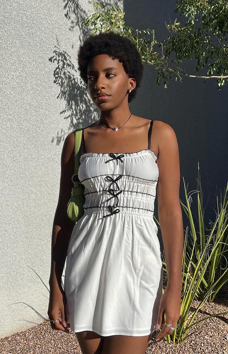 Close-up of the white mini dress showing the shirred bodice with black lace-up detail and small black bows